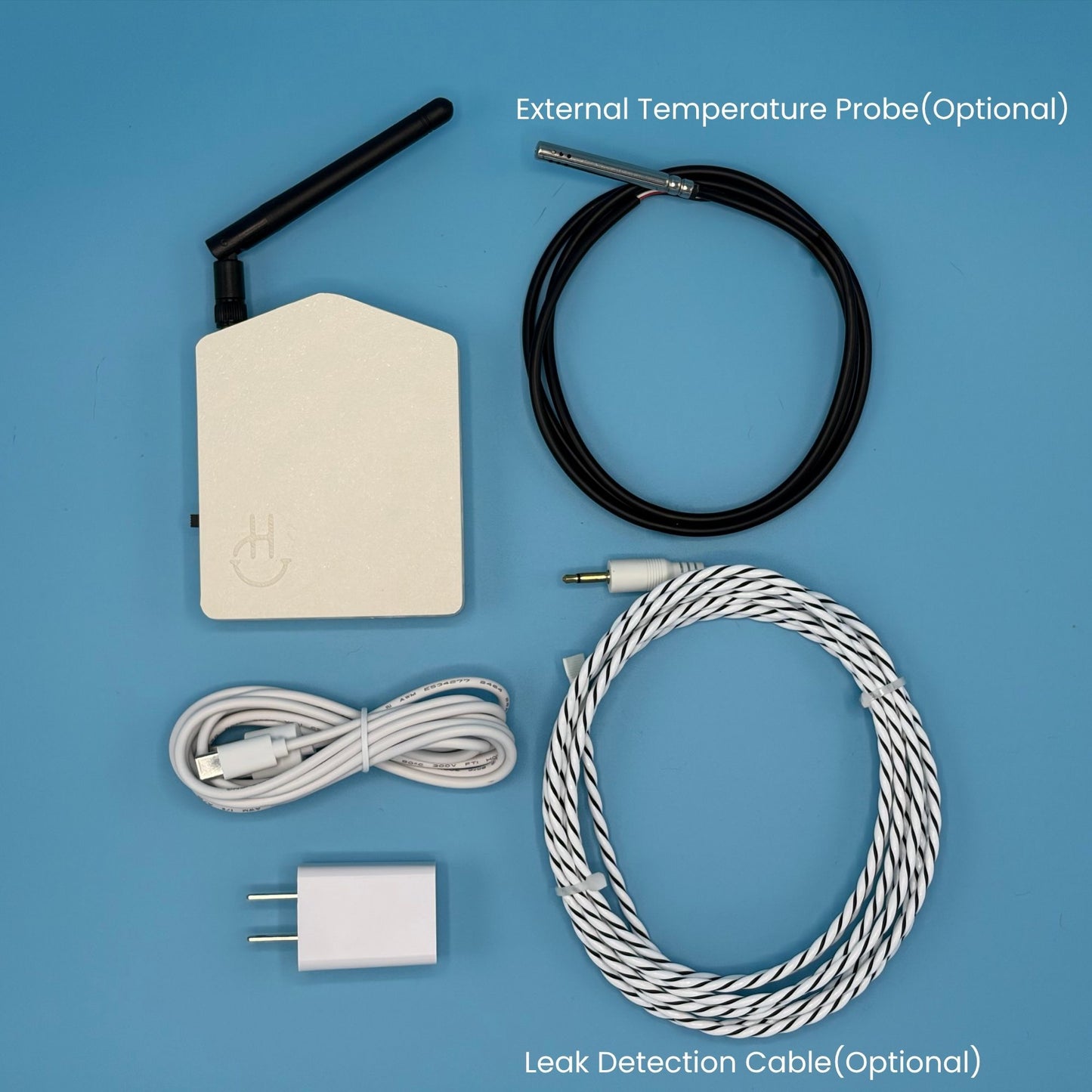 A smart home temperature and humidity sensor kit with its accessories laid out on a solid blue background. The kit includes a white electronic sensor box with a black antenna, an optional black external temperature probe cable, a white USB charging cable, a white wall charger, and an optional white-and-black leak detection cable.